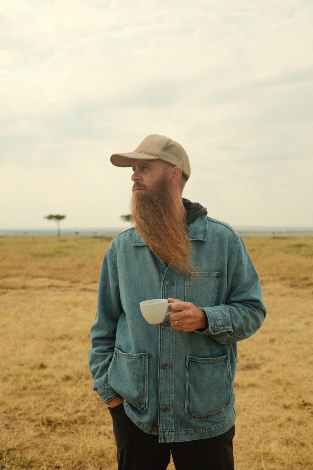 Jon Hartman outdoors with a cup, wearing a denim jacket and cap