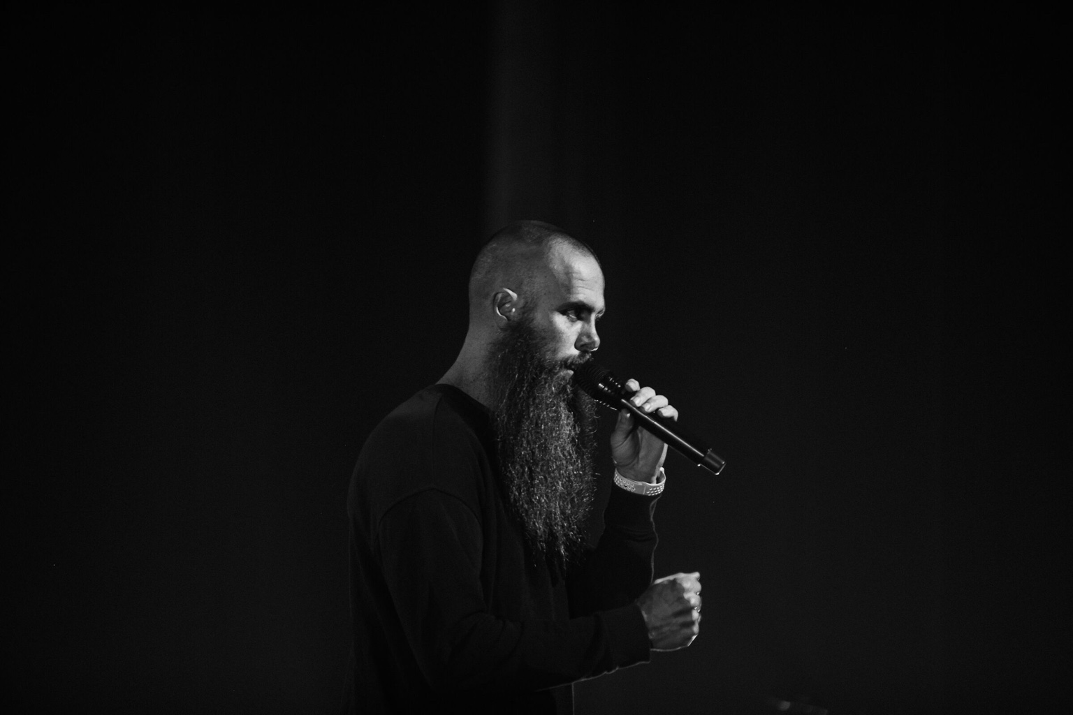 Jon Hartman holding a microphone on stage, photographed in black and white